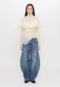 Διαφανής λευκή τοπ με ριχτές λεπτομέρειες, φορεμένο πάνω από τζιν παντελόνι. Σχεδίαση με φαρδύ πόδι, μπλε ύφασμα με ξεθωριασμένο φινίρισμα και μαύρα παπούτσια.