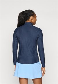 Marineblå langermet topp med teksturert mønster, høy krage og tettsittende design, parret med et lys blått utsvingt skjørt. Synlige sømmer og stitching.