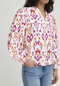 Multi-color blouse featuring a floral ikat pattern in pink, orange, and white, with a v-neck, gathered sleeves, and a relaxed fit.