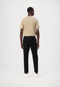 Camisa curta bege, calças pretas ajustadas e ténis brancos. A camisa tem um design simples, enquanto as calças apresentam um bolso nas costas.