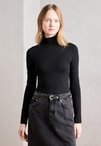 Top a maniche lunghe nera con collo a imbuto abbinato a una gonna in denim nera a vita alta. La gonna è dotata di una cintura nera con una fibbia argentata.