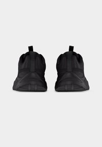 Paire de chaussures de sport noires vues de dos sur un fond uni clair avec des languettes sur le col du talon.