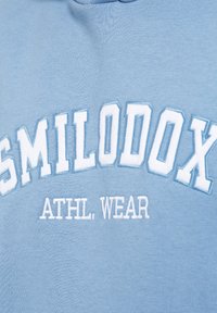 Sudadera azul claro con bordado en relieve de color blanco que dice "SMILODOX ATHL. WEAR," con un tejido texturizado.