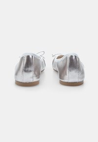 Silberne, metallische Ballerinas mit glatter Textur, runder Zehenform und Schnürdetails, die ein dezentes genähtes Design auf der Rückseite aufweisen.