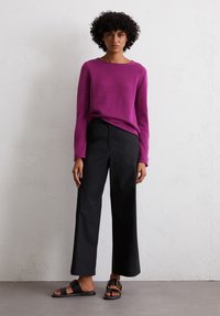 Fuchsia Strickpullover mit Rundhalsausschnitt, kombiniert mit schwarzen, weit geschnittenen Hosen und schwarzen Sandalen mit goldener Schnalle. Strukturiertes Material.