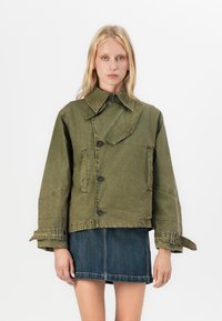 Olivengrønn kort jakke, teksturert stoff, stor krage, knappeåpning, sidelommer, justerbar belte på ermene, brukt med denimskjørt.