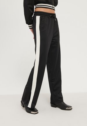Pantalons de sport noirs avec une bande latérale blanche, taille élastique et cordon de serrage. Fabriqués en tissu lisse avec une coupe décontractée et des fentes aux chevilles.