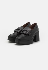 Zapatos de plataforma de cuero negro con punta redonda, correas anchas con hebillas y un tacón grueso con superficie texturizada.