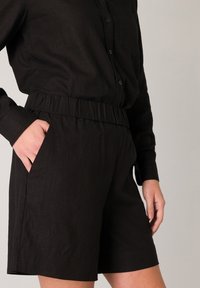 Zwarte shorts met een elastische tailleband, zijzakken en een gladde, lichtgewicht stof. Het ontwerp is eenvoudig met een getailleerde pasvorm.