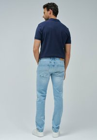Polo navy combinado con jeans de un azul claro. Los jeans tienen un corte clásico y detalles en el bolsillo trasero, complementados con zapatillas blancas.