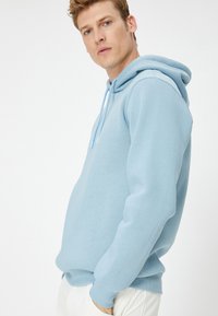 Sudadera azul claro de tela suave, con un bolsillo tipo canguro, capucha ajustable con cordón y puños y dobladillo acanalados.