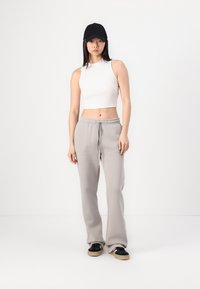 Hallide hallid püksid elastse vöökohtaga, millele on lisatud valge lühike tank top. Must müts täiendab musti tossusid, millel on pruunid tallad.