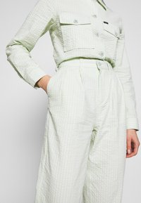 Light green striped shirt and matching wide-leg pants made of textured fabric. Features two front pockets and button-up design.