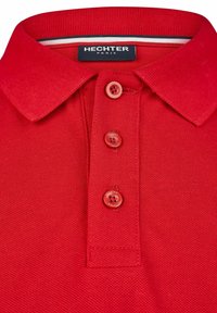 Rotes Polohemd aus strukturiertem Strick mit Kragen, drei roten Knöpfen und einem dezenten Markenetikett innen am Kragen.