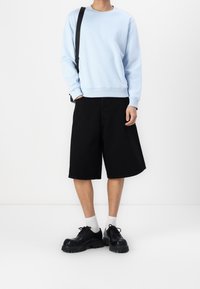 Sweat-shirt bleu clair à manches longues, short large noir et chaussures noires épaisses. Les chaussettes sont blanches. Design simple et minimaliste.