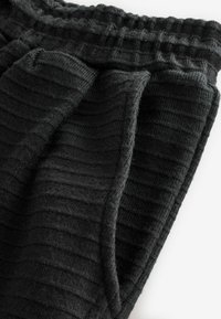 Schwarze, gerippte Jogginghosen mit strukturiertem Finish, ausgestattet mit einem elastischen Bund und Seitentaschen. Das Material wirkt weich und warm.