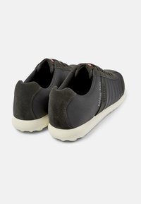Scarpe da ginnastica nere con tomaia sintetica liscia e accenti in pelle scamosciata. Presentano un design ondulato e una suola bianca a contrasto.