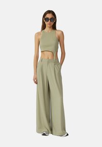 Světle zelený žebrovaný crop top s vykrojením spárovaný s širokými kalhotami s vysokým pasem ve stejném materiálu. Zahrnuje sluneční brýle a tenisky.