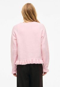 Rosa strikket genser med rund hals og volangkant nederst. Teksturen er myk, med lange ermer og en avslappet passform.