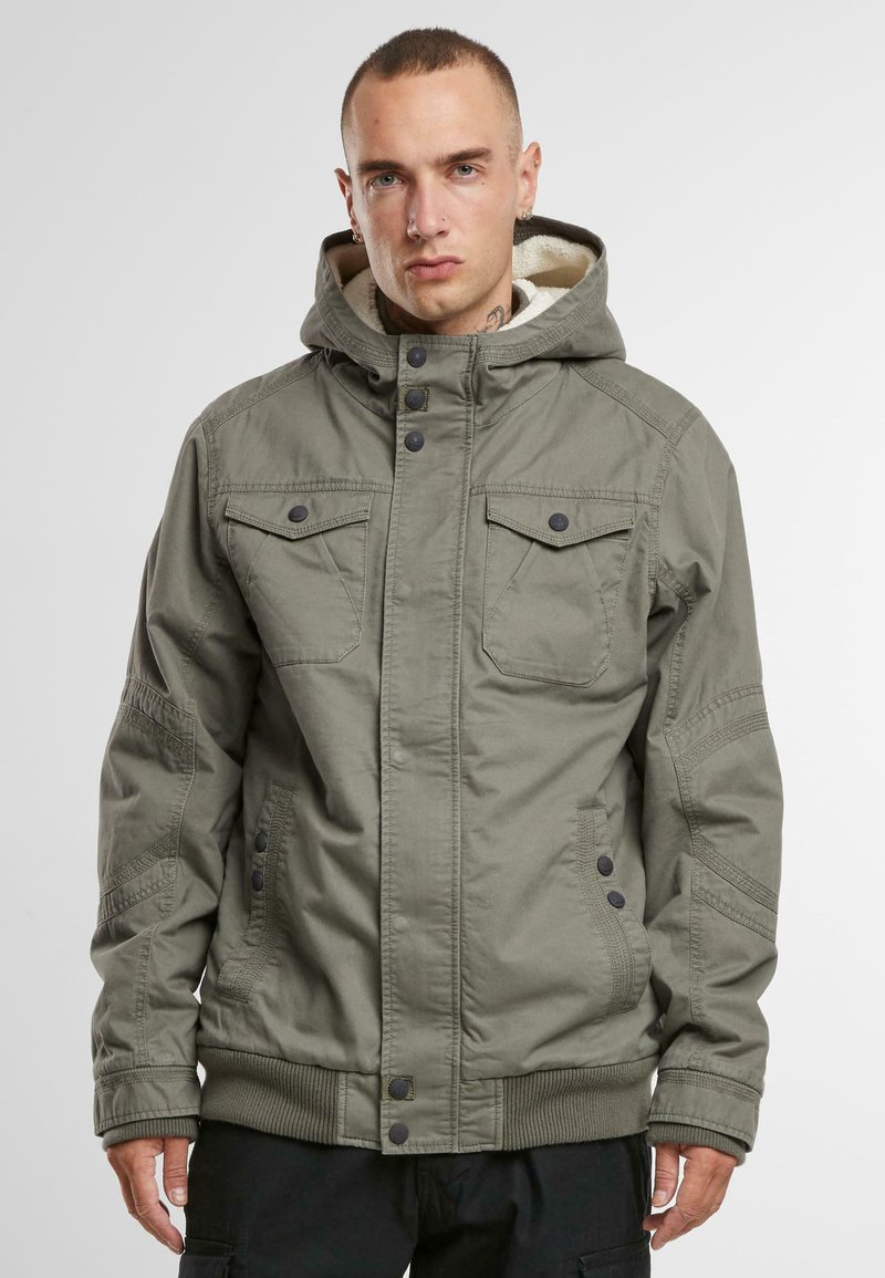 Chaqueta con capucha de color verde oliva, con forro de forro polar, dos bolsillos en el pecho y cierres de botones a presión. Presenta puños y dobladillo acanalados.