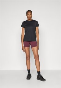 Fekete rövid ujjú póló bordó sportnadrággal. A modell fekete sportcipőben és zokniban áll, semleges háttér előtt.