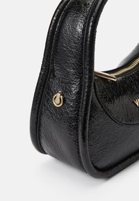 Borsa a tracolla in pelle nera con una finitura liscia e testurizzata; presenta una cerniera dorata e un dettaglio hardware circolare sul lato. Forma compatta.
