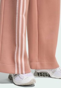 Ružičaste hlače ležernog kroja od mekanog materijala imaju bijele bočne pruge i široke nogavice. Uparene s bijelim atletskim cipelama koje imaju zračno udobnost.