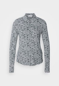 Chemise à manches longues noire et blanche à pois, boutonnée avec col, coupe ajustée, présentée sur un fond clair uni.