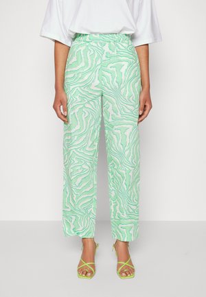 Calças verdes e brancas com padrão, com um cós elástico, apresentando um corte largo e uma textura suave. Combinadas com sandálias verdes com tiras.
