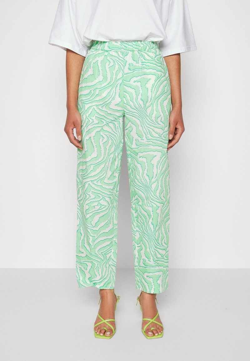 Calças verdes e brancas com padrão, com um cós elástico, apresentando um corte largo e uma textura suave. Combinadas com sandálias verdes com tiras.