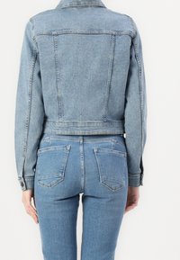 Jasnoniebieska kurtka dżinsowa o dopasowanym kroju, z długimi rękawami i zapięciem na zatrzaski. Noszona z wysokim stanem dopasowanymi dżinsami.