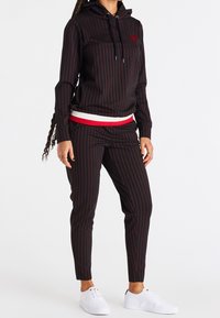 Sudadera con rayas negras y rojas, con un dobladillo acanalado, combinada con pantalones a juego. Presenta cordones y acentos en blanco. Zapatillas blancas completan el look.