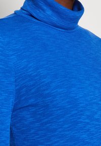 Maglione blu a collo alto con un motivo di lavorazione a maglia testurizzato. Il materiale è morbido, con una vestibilità aderente attorno al collo e una finitura liscia.