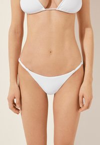 Vitt bikini-set med en triangulär topp och minimal täckning på botten. Slät tyg med knytningar på sidorna av bikiniunderdelen.