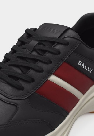 Baskets en cuir noir avec lacets noirs, bandes latérales rouges et blanches, texte "BALLY" sur le côté, et une semelle blanche visible en dessous.