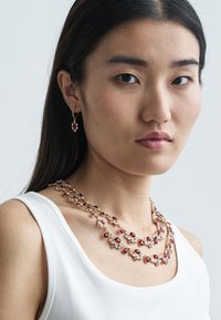 Rode en heldere edelsteen ingelegde gelaagde ketting met goudkleurige ketting, gecombineerd met bijpassende oorhangers. Glad afgewerkt, elegant ontwerp.