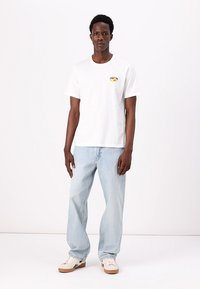 Hvitt bomull T-skjorte med korte ermer, med et fargerikt emblem på brystet. Kombinert med lyseblå denimjeans og hvite sneakers.
