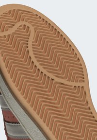 Soletta in gomma marrone con motivo a zigzag texturizzato, parte superiore in suede grigio e rosso di lato, che mostra dettagli di cucitura e contrasto di colori.