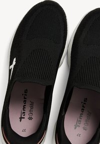 Svarta stickade sneakers med en texturerad ovandel, elastiska sidor och en vit logotyp. Har en vadderad rosa innersula och en lätt vit sula.