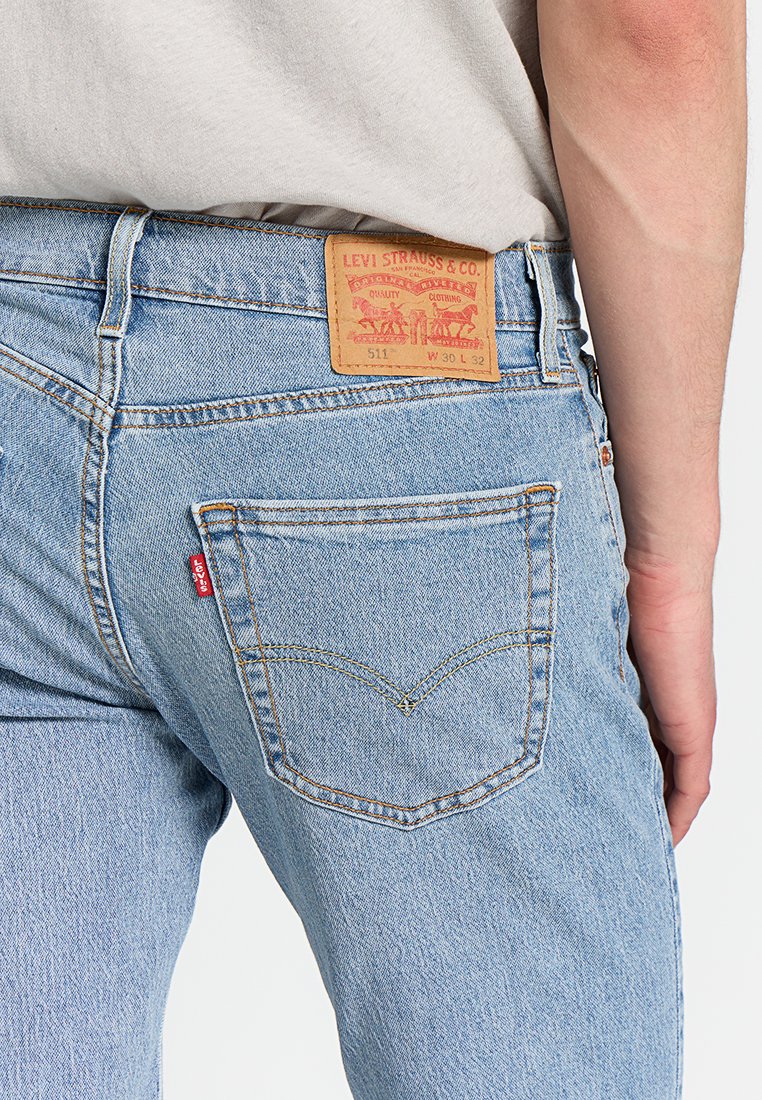 Vaqueros Levi's 511 de color azul claro en la parte baja de la espalda y la cadera de una persona, mostrando el bolsillo trasero con la etiqueta roja de Levi's y la etiqueta de cuero de la marca en la cintura.