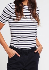 Camisa de manga corta a rayas en azul marino y gris claro, con rayas horizontales y un diseño ajustado. Tejido suave con cuello redondo.