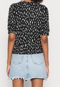 Schwarzes Oberteil mit weißem unregelmäßigem Punktmuster, kurzen Ärmeln und einem lockeren Schnitt, kombiniert mit einem verblassten Denim-Minirock mit rohem Saum.