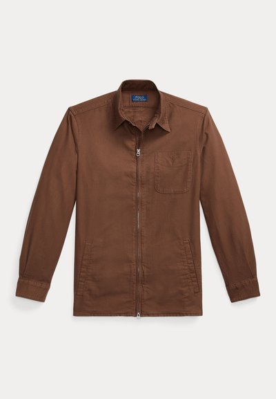 Chaqueta marrón con cremallera hecha de algodón, con cuello tipo camisa, un bolsillo en el pecho y bolsillos laterales. Textura suave y mangas ajustadas.