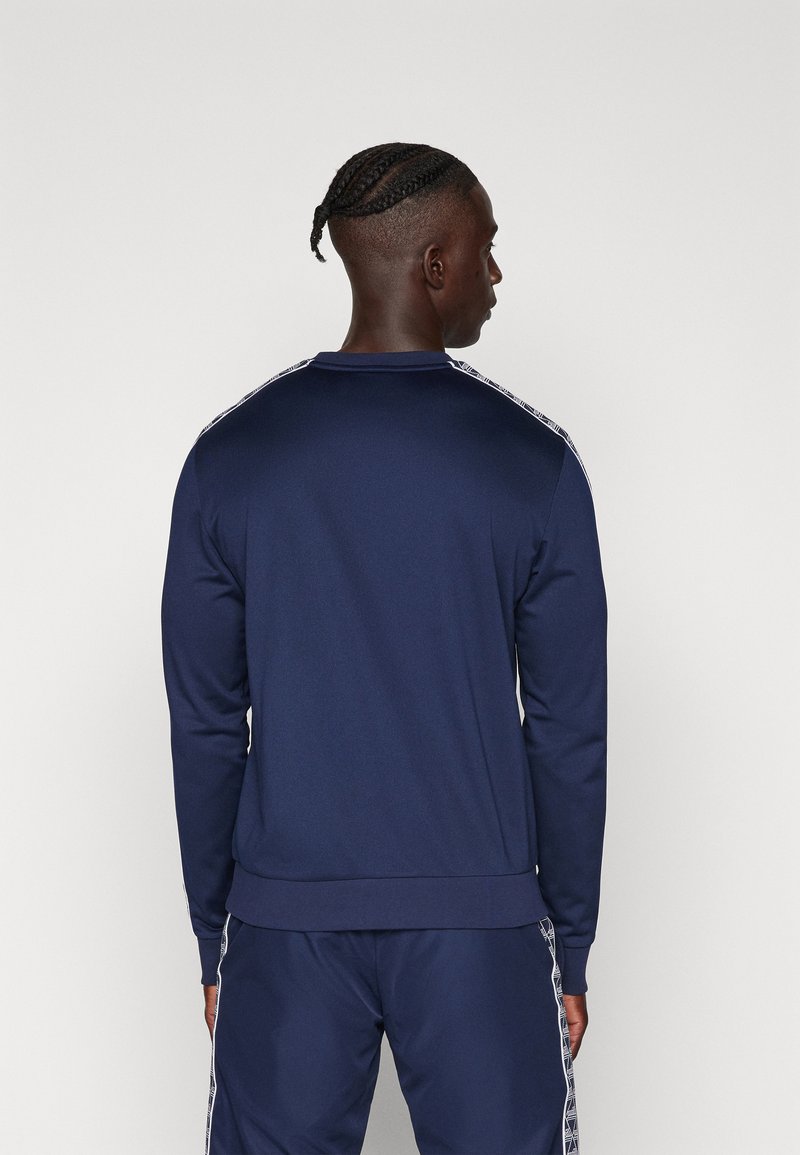 Felpa navy con maniche lunghe, polsini a costine e scollo a girocollo. Strisce laterali notevoli con un motivo geometrico. Tessuto liscio e elasticizzato.