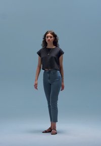 Melna īsa T-krekla, gaisas zilas džinsa bikses ar augstu jostasvietu un melnas sandales. Modelei ir lokainas matu šķipsnas un vienkārša kaklarota.