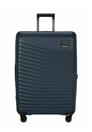 Valise rigide bleu foncé à motif ondulé horizontal, quatre roues, poignée télescopique déployée, et logo Samsonite en haut à droite.