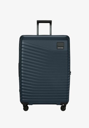 Valise rigide bleu foncé à motif ondulé horizontal, quatre roues, poignée télescopique déployée, et logo Samsonite en haut à droite.