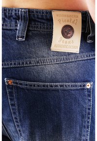 Jeans aus Denim in dunkelblauer Farbe, mit einem Lederetikett, das "Picaldi Jeans Authentic Design" trägt, und Kupfernieten an den Taschen.