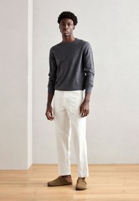 Grå sweater, hvide bukser og brune klipklapper. Sweateren har rund hals, ribbede ærmer og kant. Bukserne har en løs pasform og lommer.