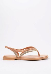 Sandalias planas con una suela suave de color durazno y tiras trenzadas. Acento texturizado en oro en el diseño superior. Minimalistas y ligeras.